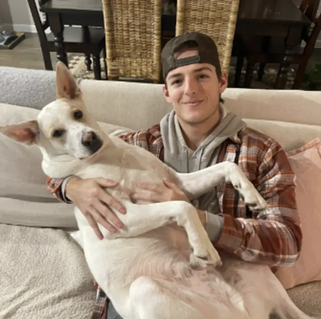 Man in cap holding small dog close to his face